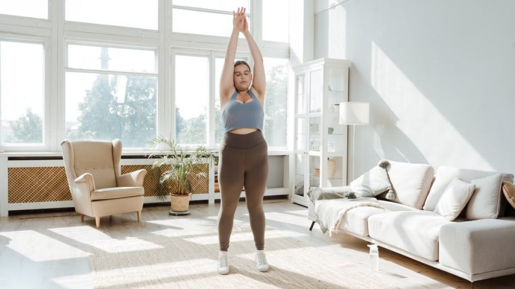 A woman practices stretching exercises in a sunlit living room, promoting wellness and healthy lifestyle.